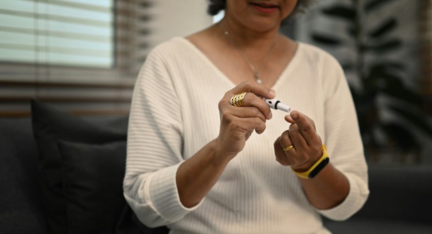 Diabetic senior woman taking blood sample with lancet pen. Diabetes and health care concept.